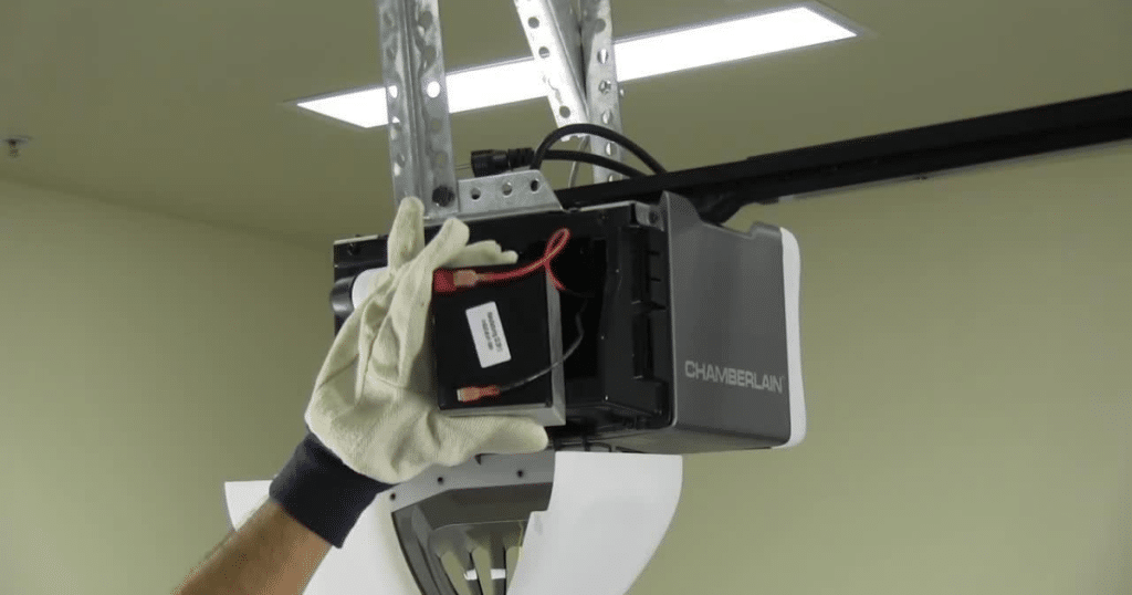 Gloved hand installs garage door opener battery.